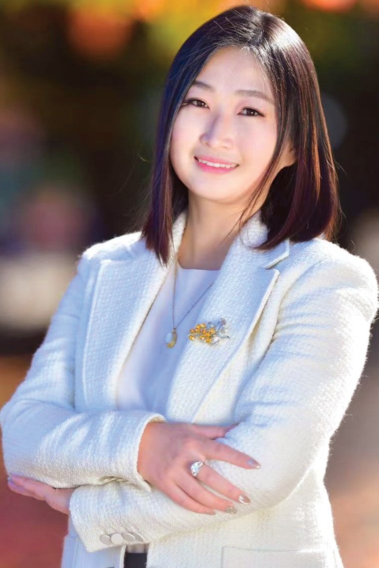 Avery Quan，身穿白色西装外套，面带微笑，背景是秋天的树